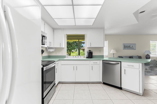 kitchen with light tile patterned floors, stainless steel appliances, a peninsula, open floor plan, and light countertops