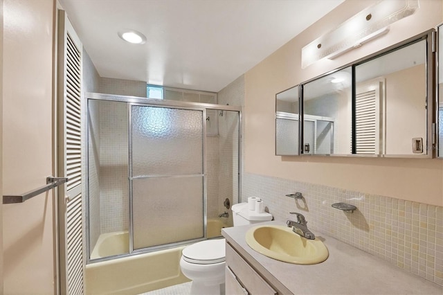 full bathroom with tile walls, shower / bath combination with glass door, vanity, and toilet