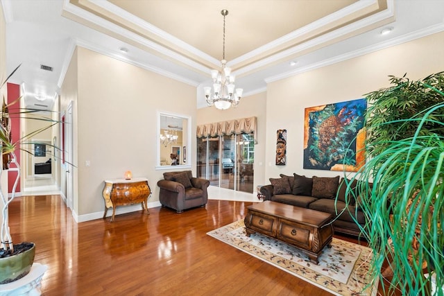 living room with a raised ceiling, ornamental molding, an inviting chandelier, and wood-type flooring