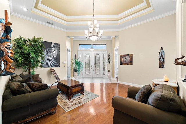 living room featuring hardwood / wood-style flooring, a raised ceiling, and decorative columns