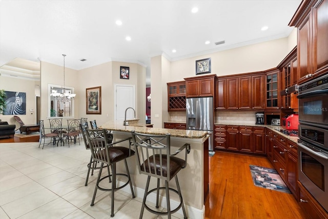 kitchen with a kitchen island with sink, hanging light fixtures, stainless steel fridge with ice dispenser, a breakfast bar, and light stone countertops