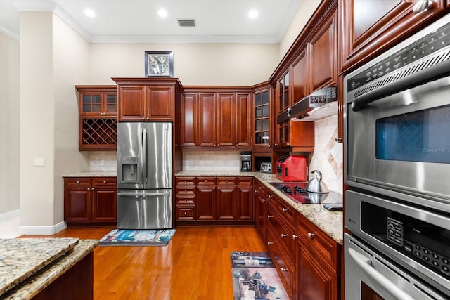 kitchen with light wood-type flooring, crown molding, stainless steel appliances, light stone countertops, and tasteful backsplash