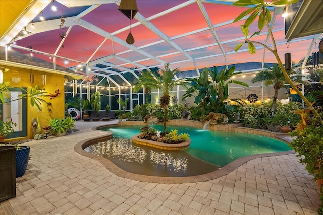 pool at dusk featuring pool water feature, a lanai, and a patio area