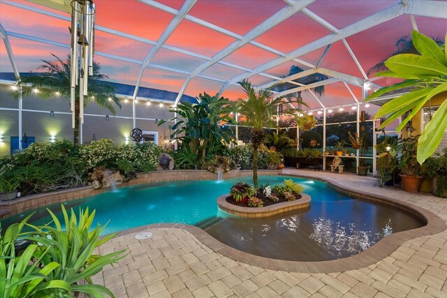 pool at dusk with a lanai, pool water feature, and a patio