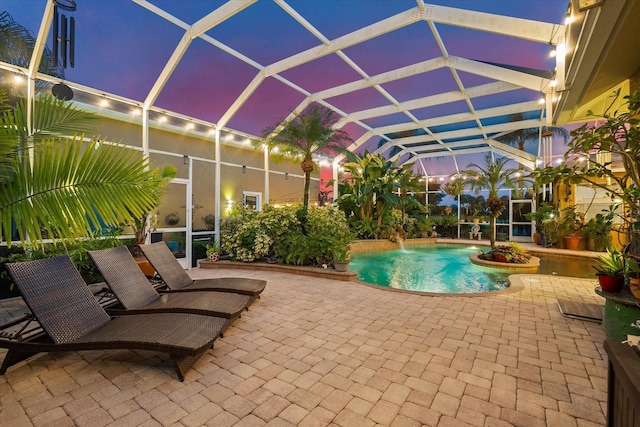 pool at dusk with a patio area, a lanai, and pool water feature