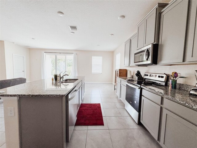 10827 Charlotte Dr, Parrish, FL 34219 - kitchen with visible vents, a kitchen island with sink, gray cabinets, a sink, and stainless steel appliances