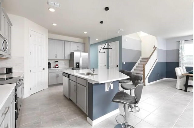 kitchen with appliances with stainless steel finishes, sink, gray cabinets, and an island with sink