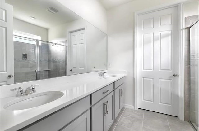 bathroom featuring a shower with shower door, double sink vanity, and tile patterned floors