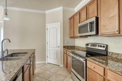 20635 Romagna Pl, Venice, FL 34293 - kitchen with stainless steel appliances, a sink, crown molding, dark stone countertops, and brown cabinetry