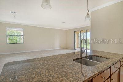 kitchen with sink, dark stone countertops, ornamental molding, tile patterned floors, and hanging light fixtures