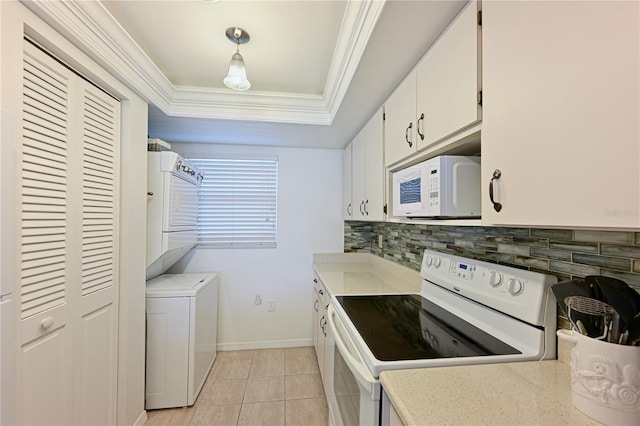 kitchen featuring white appliances, decorative light fixtures, a tray ceiling, stacked washer / drying machine, and white cabinetry