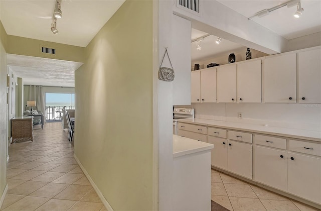 kitchen with white electric stove, white cabinets, rail lighting, and light tile patterned floors