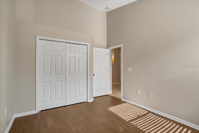 unfurnished bedroom with a closet, hardwood / wood-style floors, and a towering ceiling