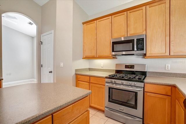 kitchen featuring light tile patterned floors, lofted ceiling, stainless steel appliances, and light brown cabinetry