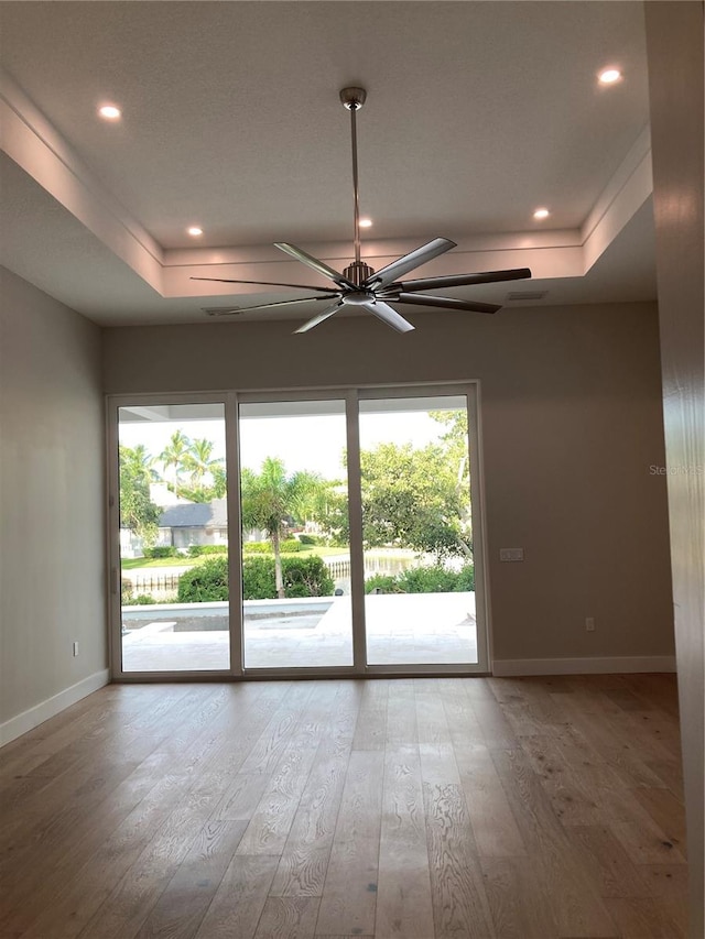 unfurnished room with wood-type flooring, a tray ceiling, and ceiling fan