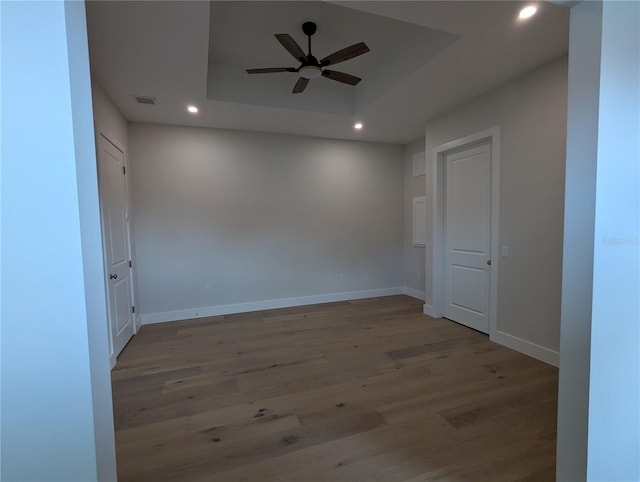 unfurnished room featuring a tray ceiling, ceiling fan, and light wood-type flooring