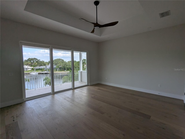 spare room featuring a tray ceiling, ceiling fan, hardwood / wood-style floors, and a water view