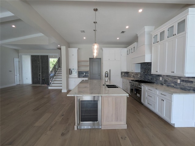 kitchen featuring range with two ovens, a spacious island, a sink, beverage cooler, and premium range hood