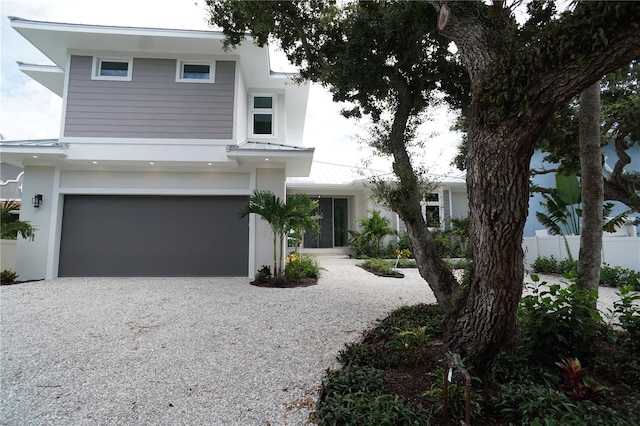 view of front facade with an attached garage, a standing seam roof, metal roof, fence, and driveway