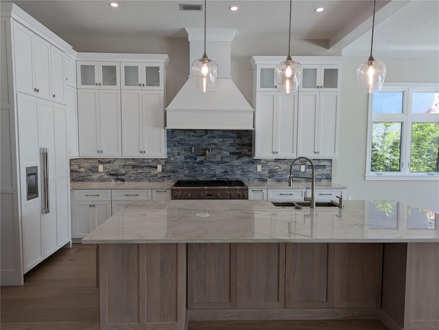 kitchen with light stone counters, sink, decorative light fixtures, a center island with sink, and white cabinets