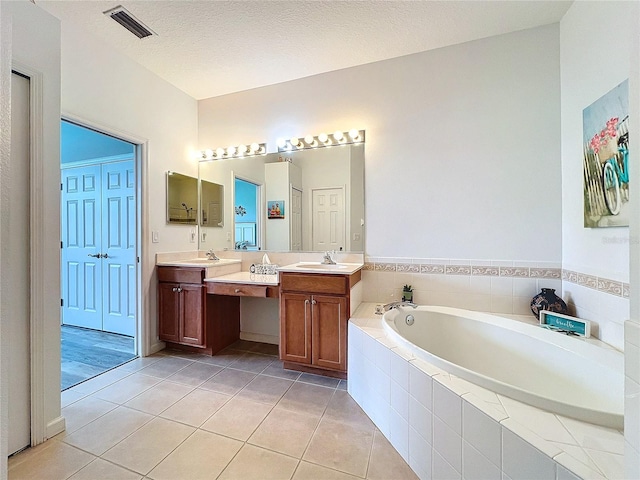 bathroom featuring tiled tub, tile patterned flooring, a textured ceiling, and dual vanity