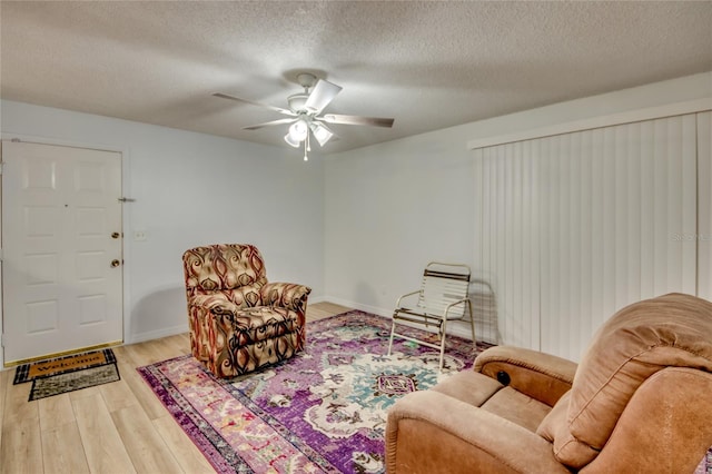 living room featuring light wood-type flooring, ceiling fan, and a textured ceiling