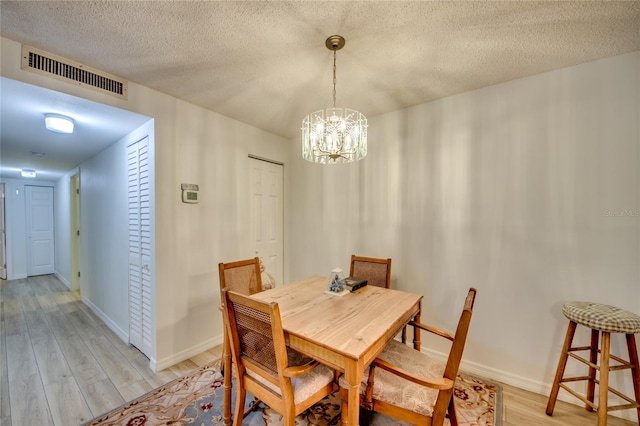 dining space with light wood-type flooring, a notable chandelier, and a textured ceiling