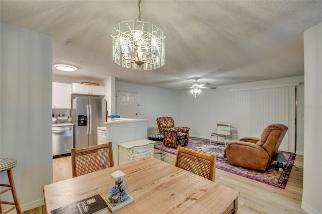 dining room featuring ceiling fan with notable chandelier, light wood-type flooring, and a textured ceiling