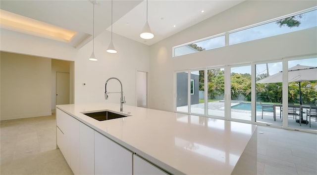 kitchen featuring modern cabinets, hanging light fixtures, light countertops, white cabinetry, and a sink