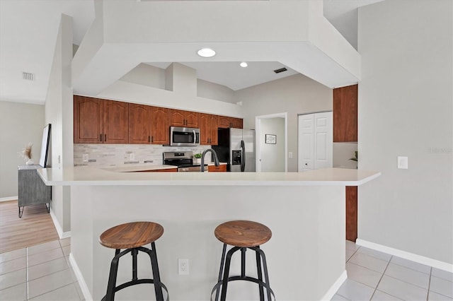 kitchen with kitchen peninsula, light tile patterned floors, stainless steel appliances, a kitchen bar, and sink