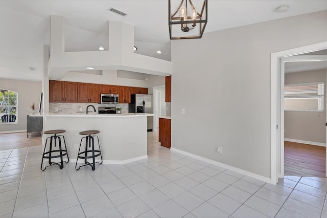 kitchen with pendant lighting, appliances with stainless steel finishes, a notable chandelier, vaulted ceiling, and decorative backsplash