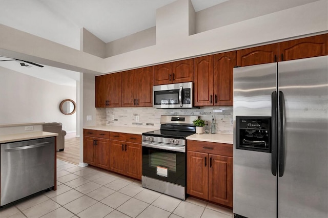 kitchen featuring light tile patterned flooring, stainless steel appliances, tasteful backsplash, and high vaulted ceiling