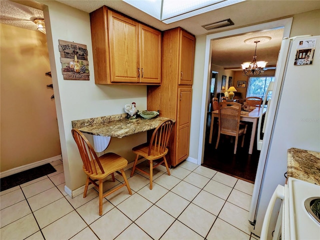 kitchen with hanging light fixtures, white refrigerator, light stone countertops, light tile patterned floors, and an inviting chandelier