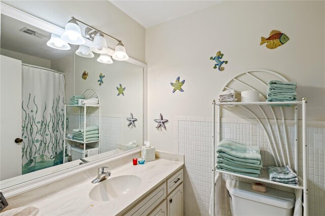 bathroom featuring vanity, toilet, and tile walls