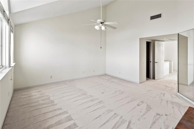 carpeted empty room featuring a barn door, high vaulted ceiling, and ceiling fan