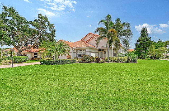 mediterranean / spanish home featuring a garage, a tile roof, driveway, stucco siding, and a front lawn