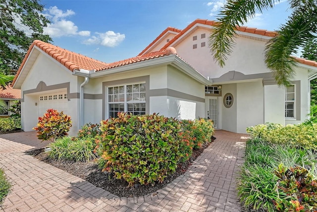 mediterranean / spanish-style house featuring a garage, a tiled roof, decorative driveway, and stucco siding