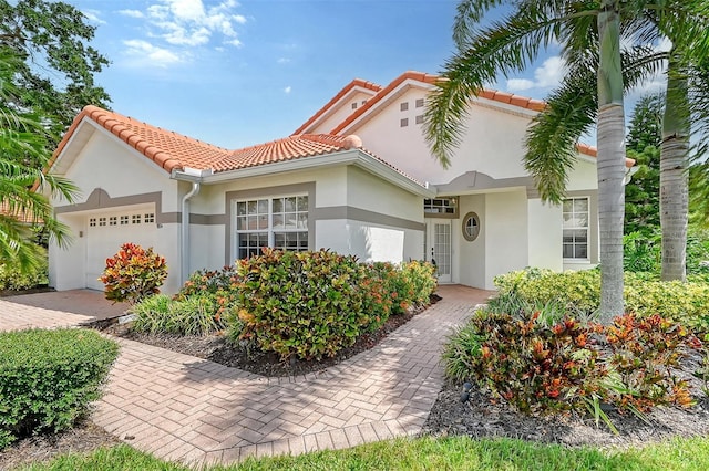 mediterranean / spanish home with a garage, a tile roof, and stucco siding