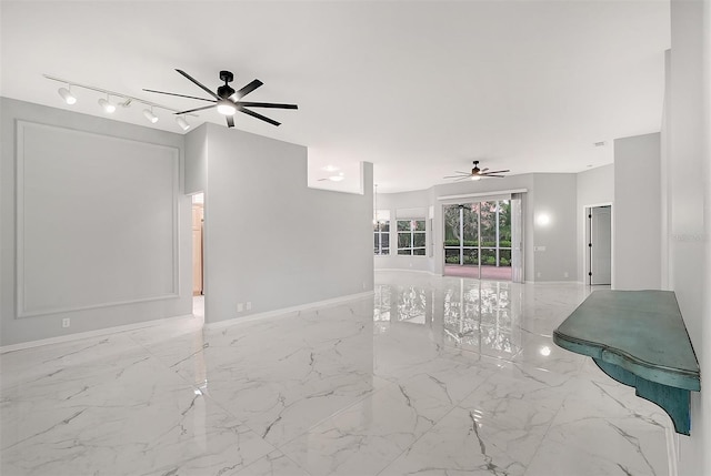 spare room featuring marble finish floor, rail lighting, ceiling fan, and baseboards