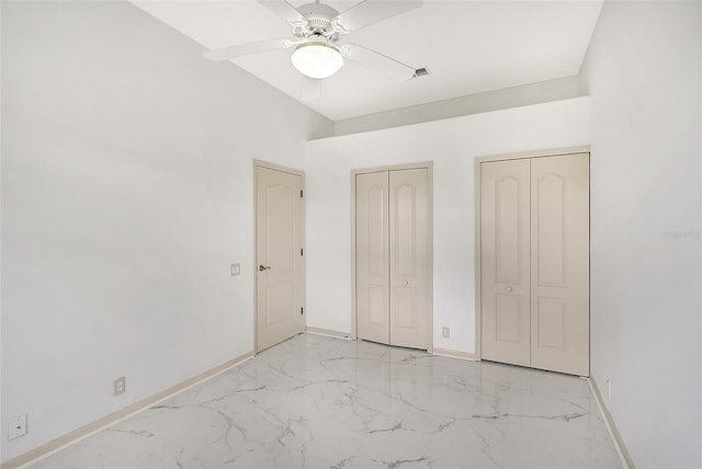 unfurnished bedroom featuring multiple closets, marble finish floor, baseboards, and a ceiling fan