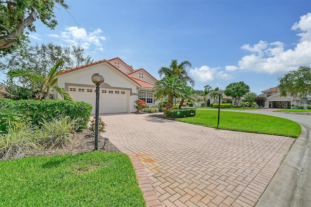 mediterranean / spanish-style house with decorative driveway, stucco siding, a garage, a tiled roof, and a front lawn