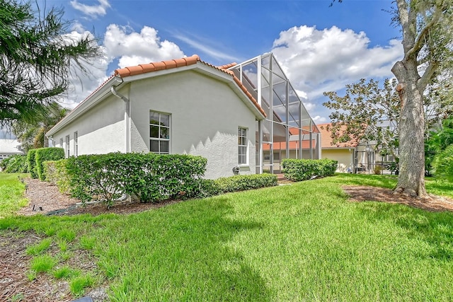 view of property exterior with glass enclosure, a lawn, a tiled roof, and stucco siding