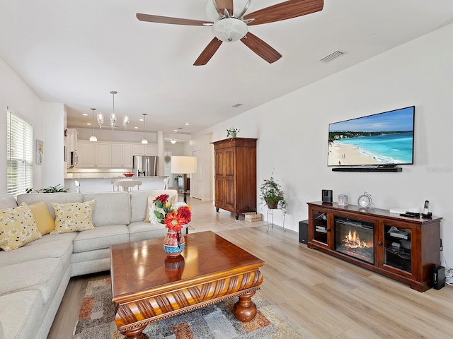 living room with ceiling fan with notable chandelier and light hardwood / wood-style flooring