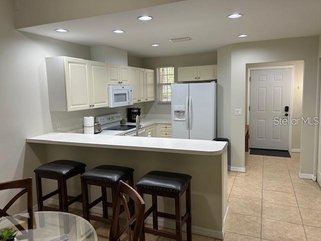 kitchen featuring light tile patterned floors, white appliances, white cabinetry, a breakfast bar area, and kitchen peninsula