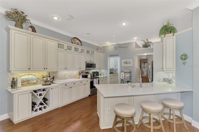 kitchen with ceiling fan, hardwood / wood-style floors, ornamental molding, kitchen peninsula, and stainless steel appliances