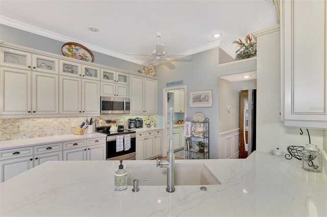 kitchen with appliances with stainless steel finishes, decorative backsplash, ornamental molding, light stone counters, and ceiling fan