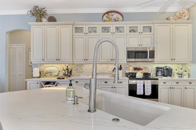 kitchen featuring appliances with stainless steel finishes, light stone counters, decorative backsplash, and ornamental molding