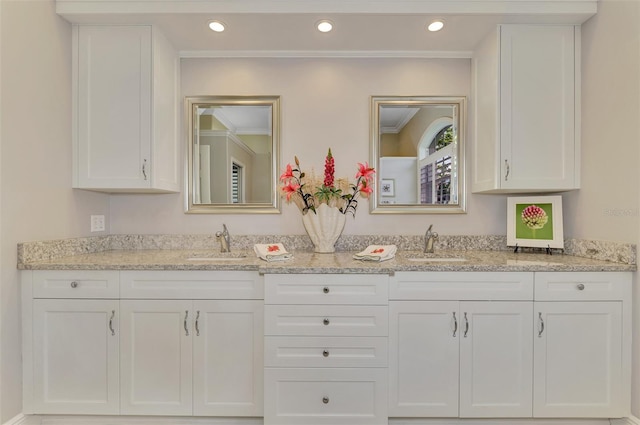 kitchen featuring sink, light stone counters, and white cabinets