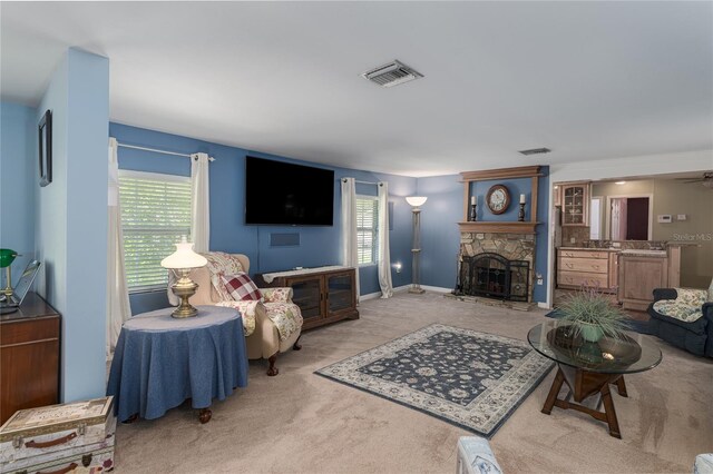 living room featuring a healthy amount of sunlight, a stone fireplace, and light colored carpet