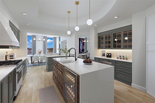 kitchen featuring sink, wine cooler, gas stove, a raised ceiling, and a center island with sink